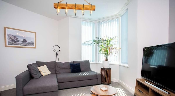 A modern living room with a grey sofa, a round coffee table, a TV on a wooden stand, a potted plant, and a framed picture on the wall. - Stylish Cosy Two Bed Apartment - Coast Location (North Tyneside)