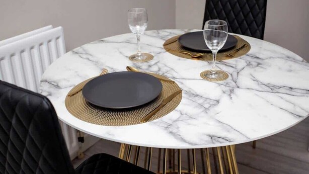 A round marble table with black plates and gold placemats, surrounded by black chairs.