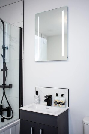 A modern bathroom with a glass shower enclosure, a white sink with black cabinets, and a large mirror above the sink.