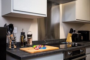 A kitchen with a black countertop, stainless steel appliances, a wooden cutting board, and various kitchen utensils.