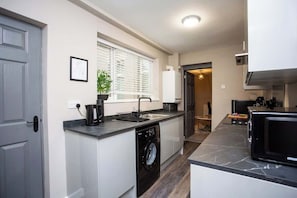 A compact kitchen with a built-in washing machine, a microwave, and a sink. - Heart of South Shields Modern Interior 2 Bed Flat (South Tyneside)
