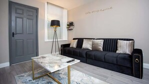 A living room with a black sofa, a marble coffee table, a floor lamp, and a door.