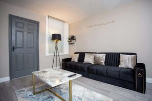 Ein Wohnzimmer mit einem schwarzen Sofa, einem Marmortisch, einer Stehlampe und einer Tür.