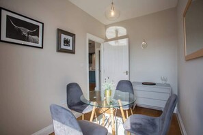 A dining area with a glass table, four chairs, a white cabinet, and two framed pictures on the wall.