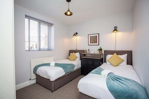 A double room with two beds, a radiator, a window, and a desk with a lamp. - Whitey Bay Coastal Bliss (Whitley Bay)