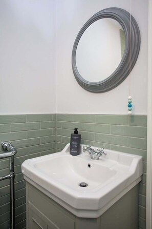 Ein Badezimmer mit einem weißen Waschbecken, einem runden Spiegel und einer grün gefliesten Rückwand.