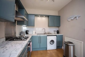 A compact kitchen with a gas stove, a washing machine, and a trash bin.