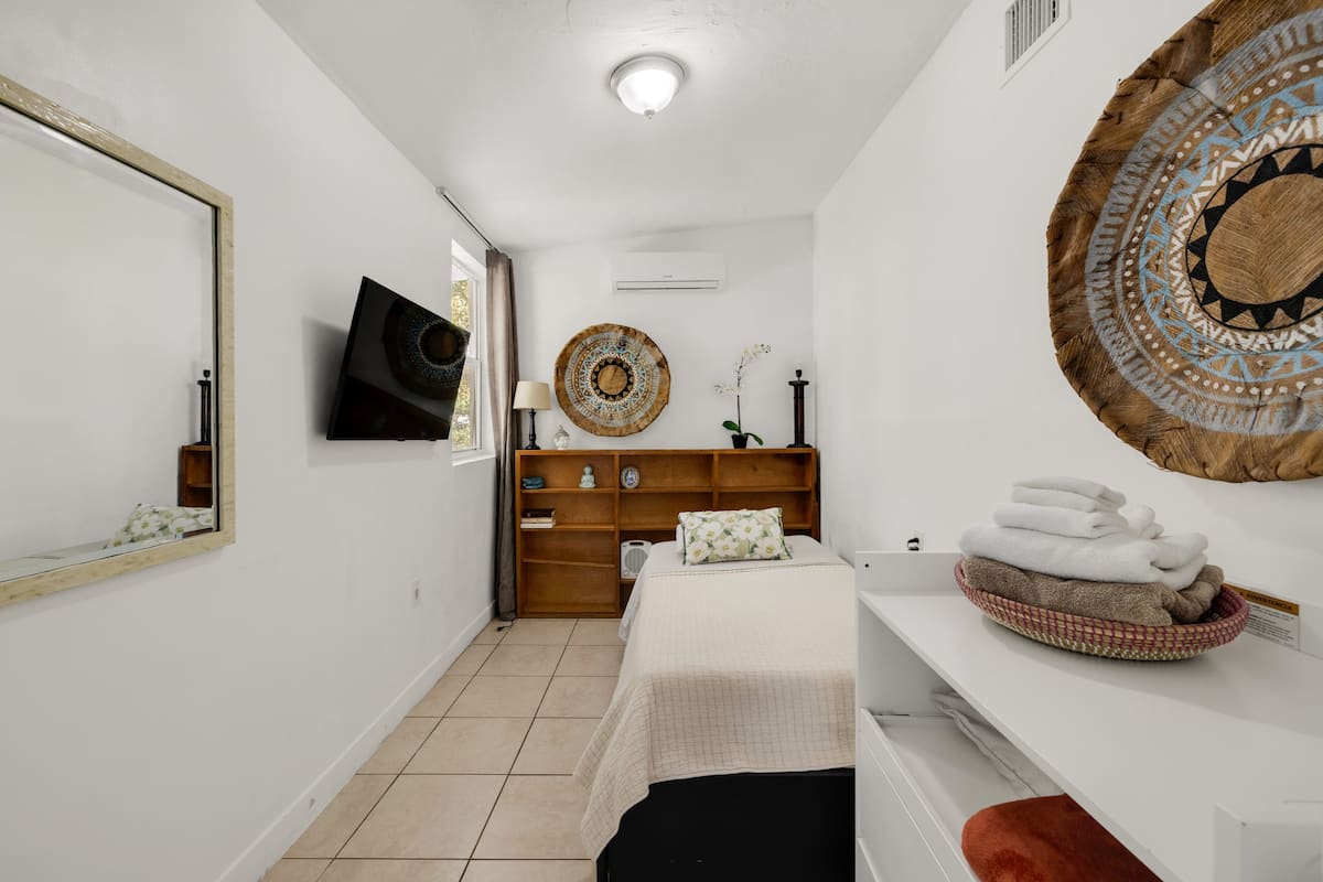 Un dormitorio con una cama, un aparador, un espejo, un televisor y un adorno en la pared.
