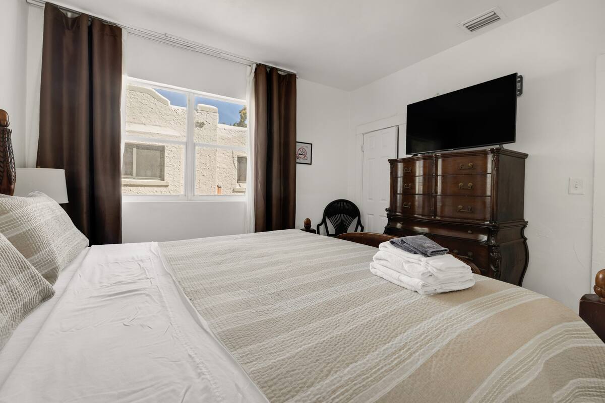 Una habitación de hotel con una cama grande, un aparador, un televisor y una ventana con cortinas.