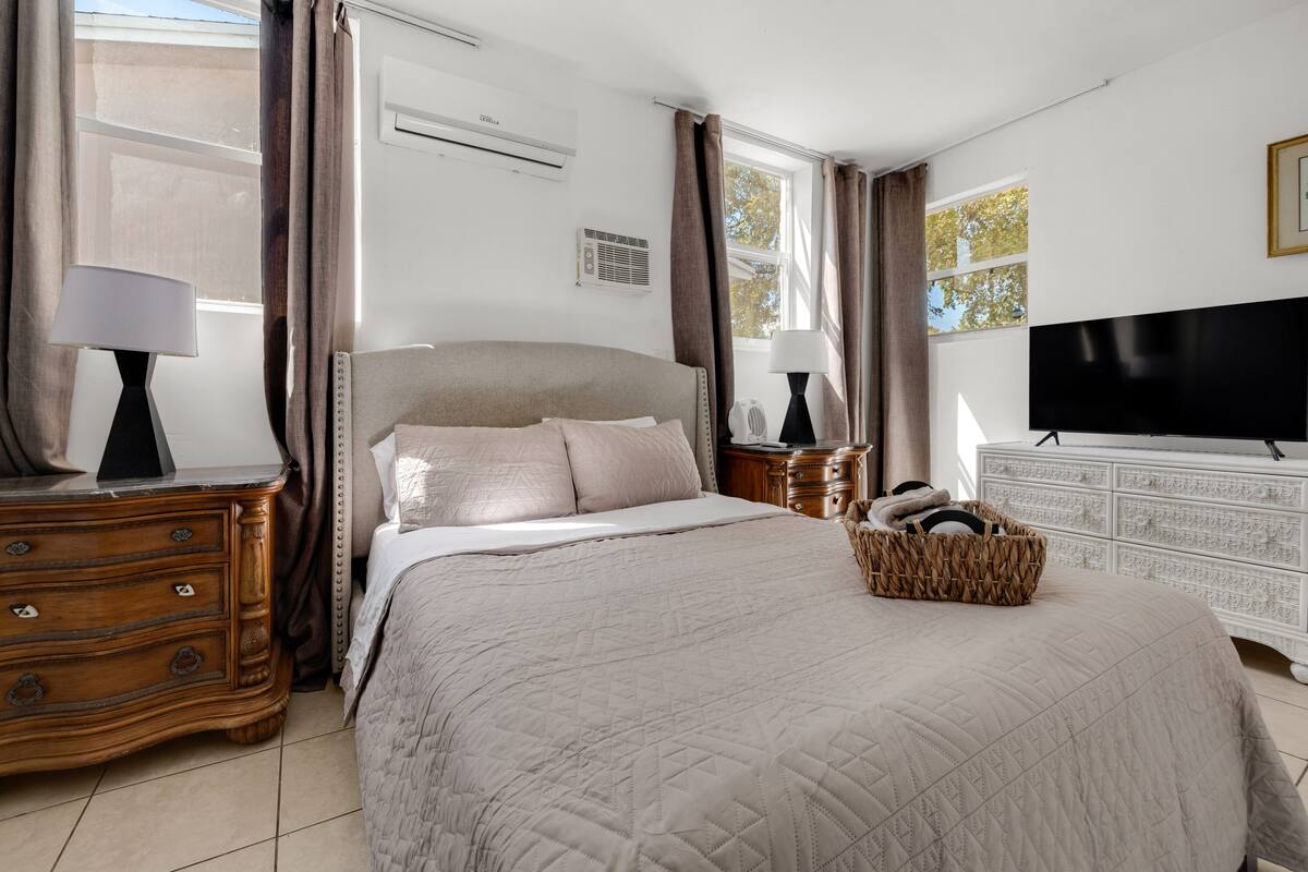 Un dormitorio con cama, cómoda, televisor y ventana con cortinas.