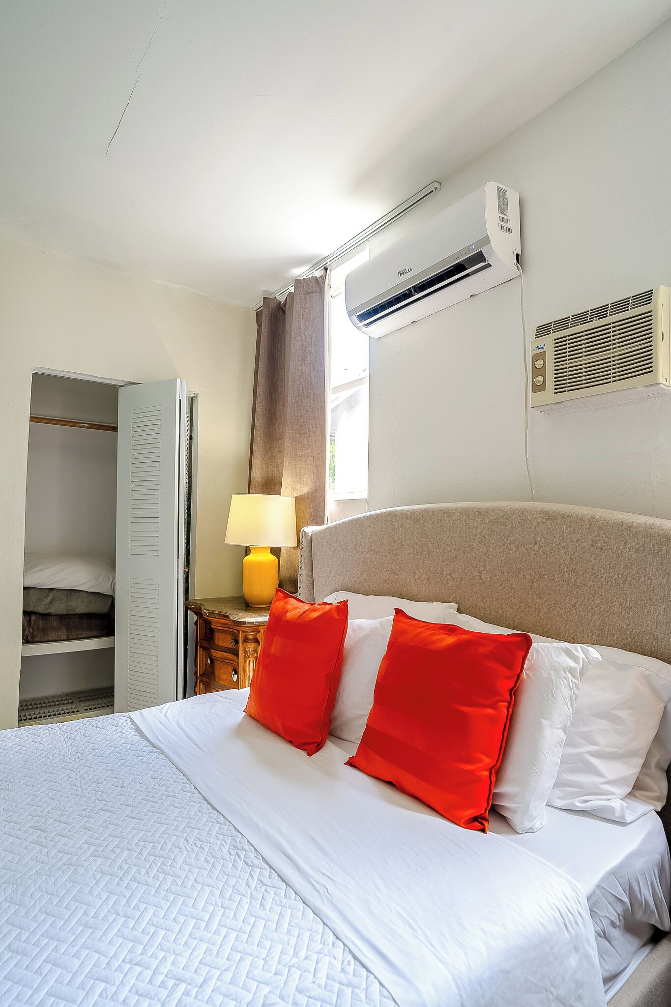 Ein Hotelzimmer mit Bett, Nachttischlampe, Klimaanlage und Kleiderschrank.