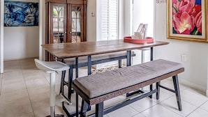Un espace repas comprenant une table en bois, un banc, un ventilateur de plafond et des œuvres d’art accrochées aux murs.