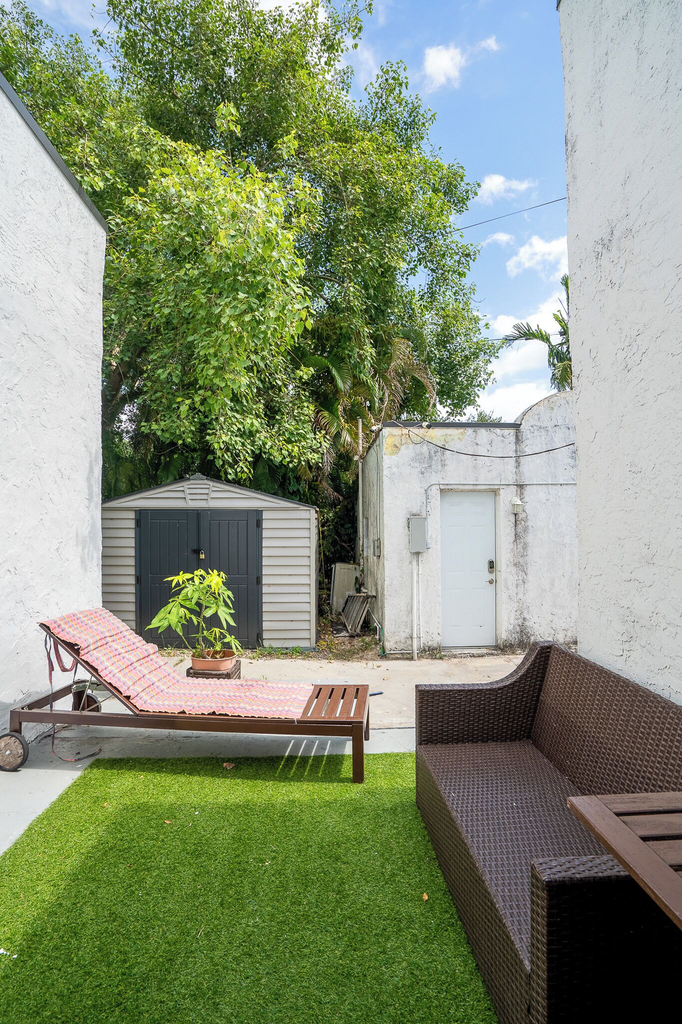 A backyard with a small shed, a covered bench, and a wicker sofa.