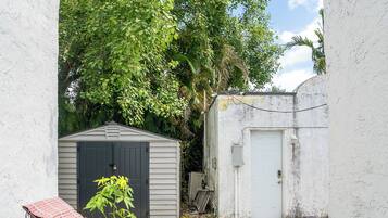 A backyard with a small shed, a covered bench, and a wicker sofa.