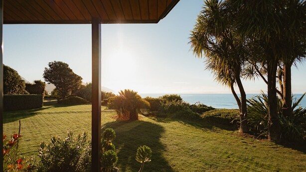 A well-maintained garden with a clear view of the ocean, a wooden pergola, and a stone pathway. - The Oceanview Suite (Hapuku)