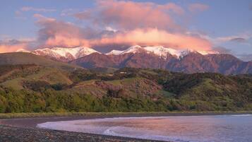 A coastal landscape with mountains in the background, a beach with pebbles, and a clear sky.