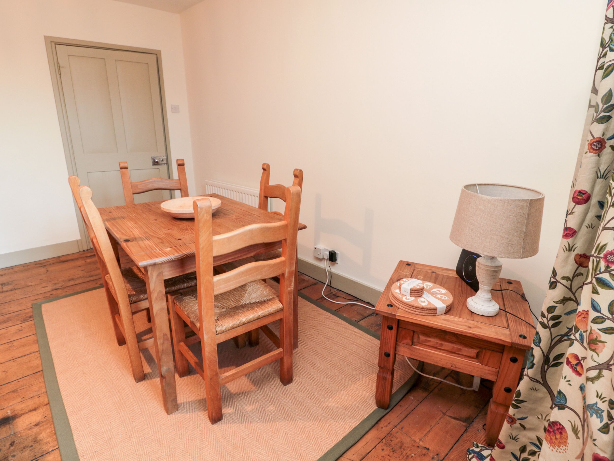 A wooden dining table with chairs, a small side table with a lamp, and a power outlet on the wall.