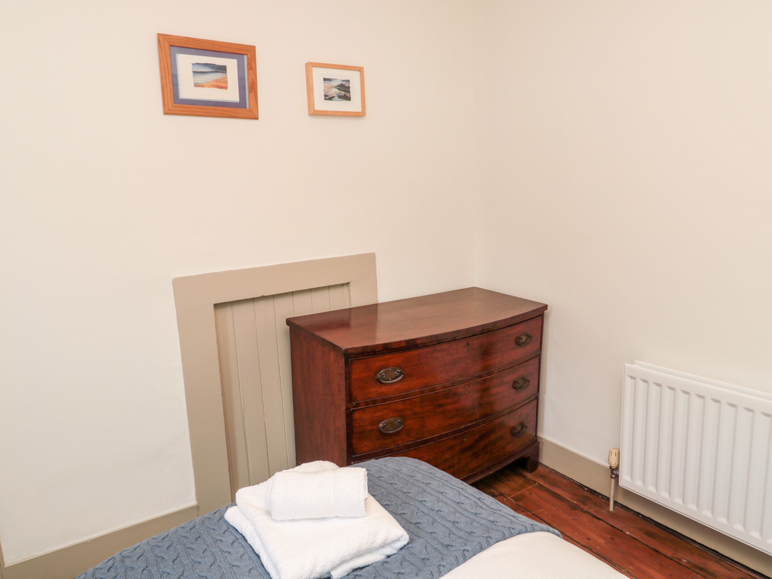 A bedroom with a wooden dresser, a bed with a blue quilt, and two framed pictures on the wall.