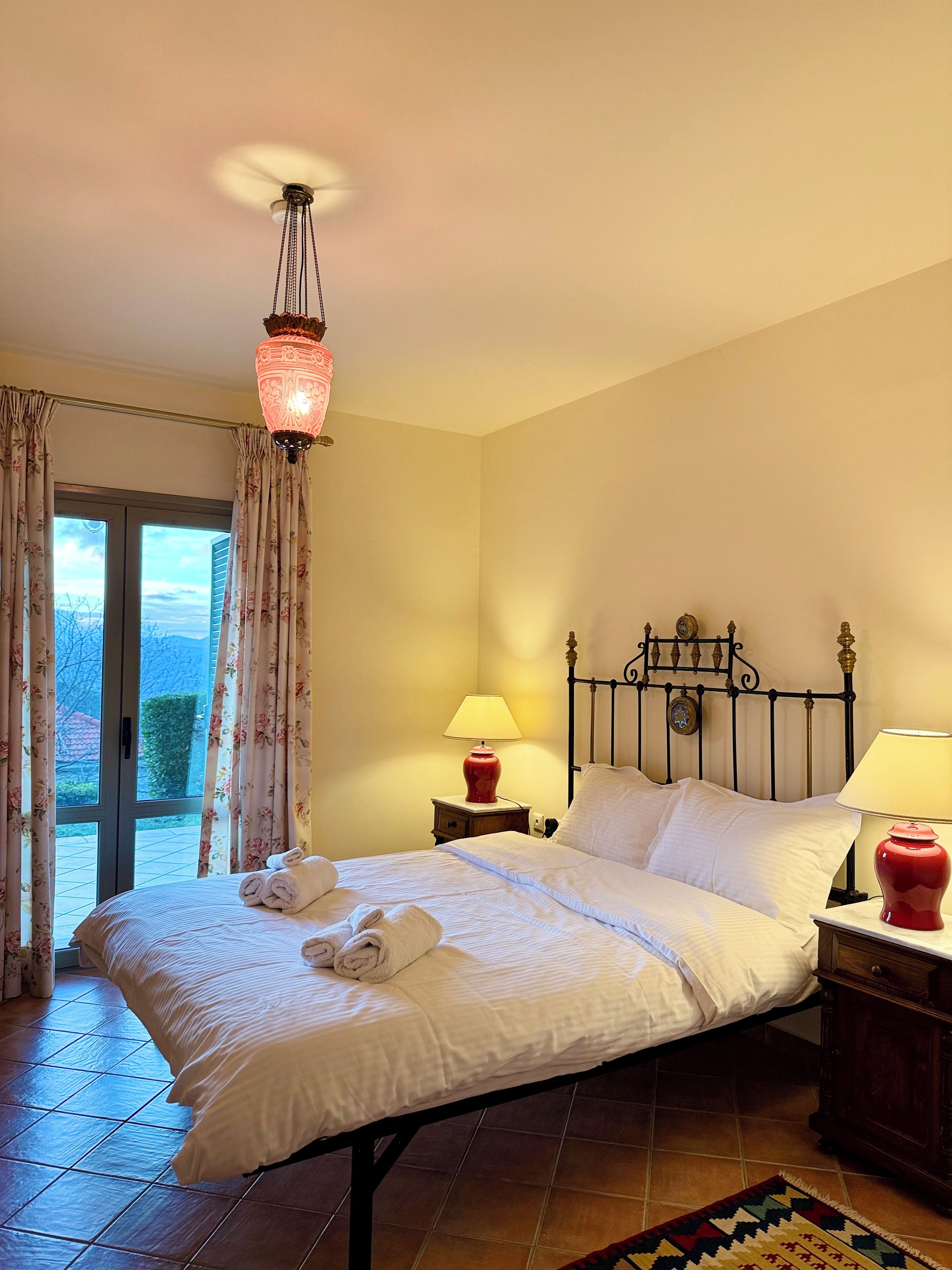 A hotel room with a bed, two bedside tables with lamps, a window with curtains, and a view of the outdoors.