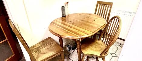 A round wooden table with four chairs, a hexagonal tiled floor, and a white wall with a power outlet.