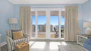A spacious living room with a view of the ocean through large sliding glass doors, a striped armchair, a small ottoman, and a coffee table.