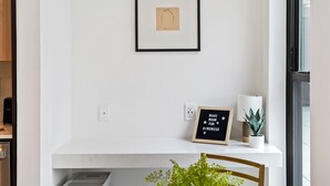 A minimalist dining area with a white marble table, a potted plant, and a framed inspirational quote on the wall. - Luxury Living in OTR:1-BR Oasis With Free Parking+Pool+Gym (Cincinnati)