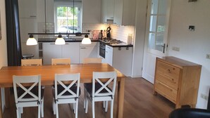 A modern kitchen with a wooden dining table and white chairs, a built-in oven, and pendant lights.