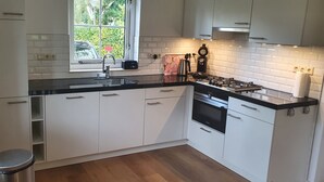 A modern kitchen with white cabinets, a black countertop, a stainless steel sink, a coffee maker, and a window with a view of greenery.