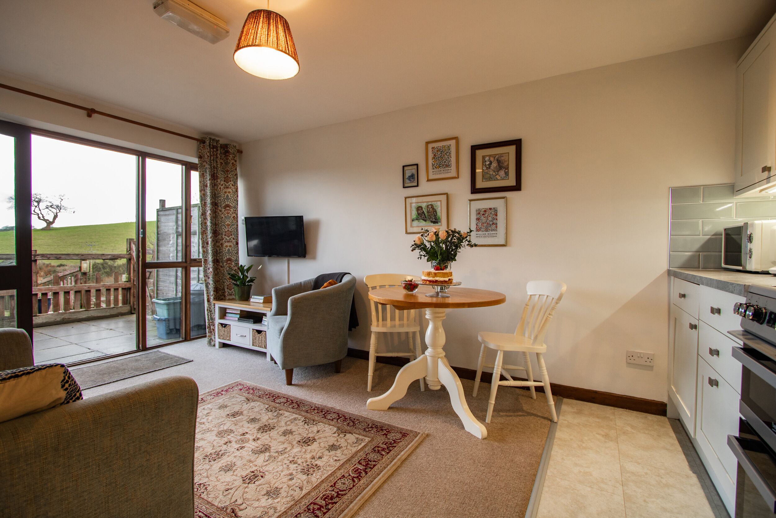 A spacious living area with a large window, a dining table with chairs, a sofa, and a kitchen area with a microwave and oven.
