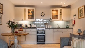 A modern kitchen with white cabinets, a built-in oven, and a dining area with a table and chairs. - The Linhay (Barnstaple)