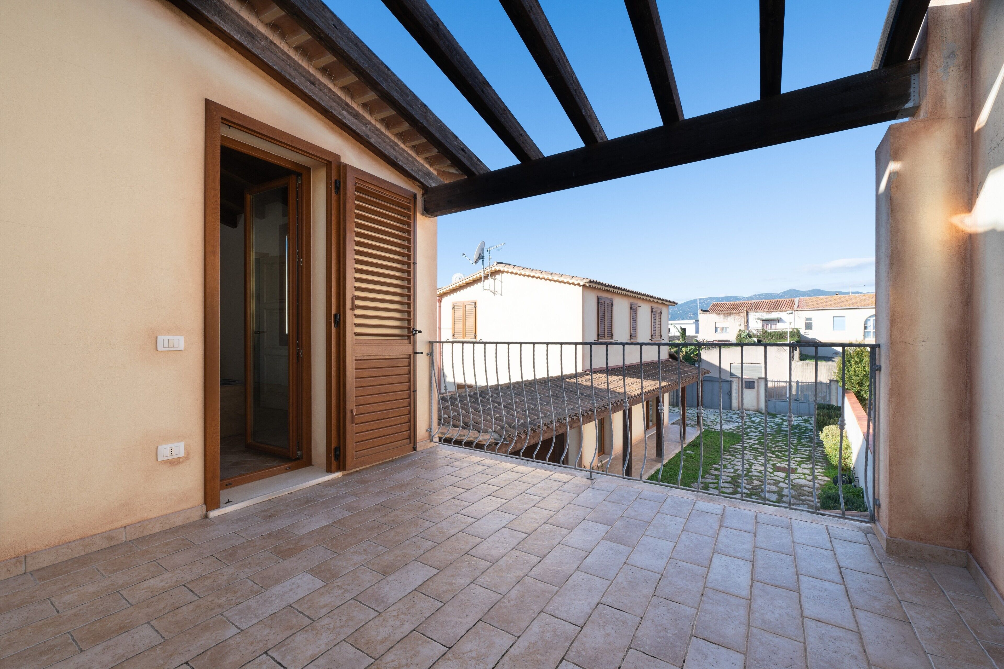 A balcony with a tiled floor, a wooden door, and a view of neighboring buildings.