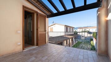 A balcony with a tiled floor, a wooden door, and a view of neighboring buildings.
