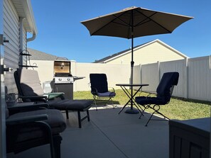 An outdoor patio with a grill, two chairs, a table, and an umbrella. - Walk to Sawgrass: Cottage Villa 2/2 - Glass Lanai/Privacy Fence, Pets Welcome! (The Villages)