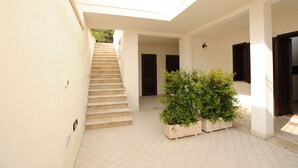 A covered outdoor area with a staircase leading to an upper level, a potted plant, and a door with a dark shutter. - Cozy apartment in pescoluse maldive del salento A6-7 (Marina di Pescoluse)