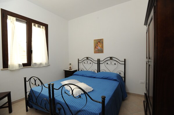 Un dormitorio con cama, mesita de noche, ventana con cortinas, un cuadro en la pared y un armario.