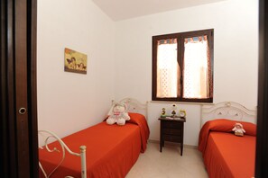 Un dormitorio con dos camas individuales, una mesita de noche, una pequeña mesa con un reloj y una ventana con cortinas.