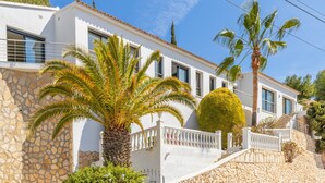A white building with stone walls, a palm tree, and a well-maintained garden.