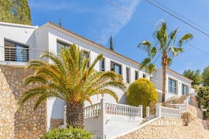 A white building with stone walls, a palm tree, and a well-maintained garden. - Villa with Sea View, Wi-Fi and Air Conditioning (Moraira)