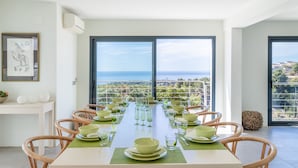 A dining area with a view of the sea, a white table, and wicker chairs.
