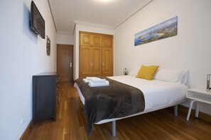 Een slaapkamer met een bed, een kledingkast, een bureau, een televisie en een schilderij aan de muur.