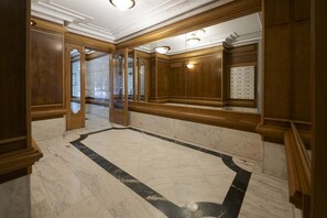 Een ruime lobby met marmeren vloer, houten lambrisering en een grote spiegel die de ruimte weerspiegelt.