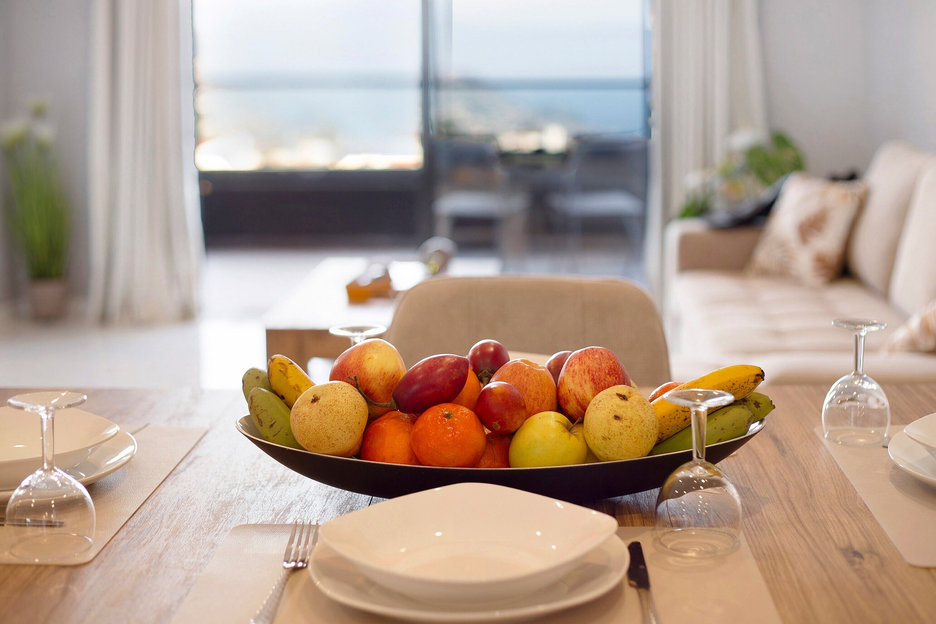 A dining table with a fruit bowl, wine glasses, and plates set for a meal.