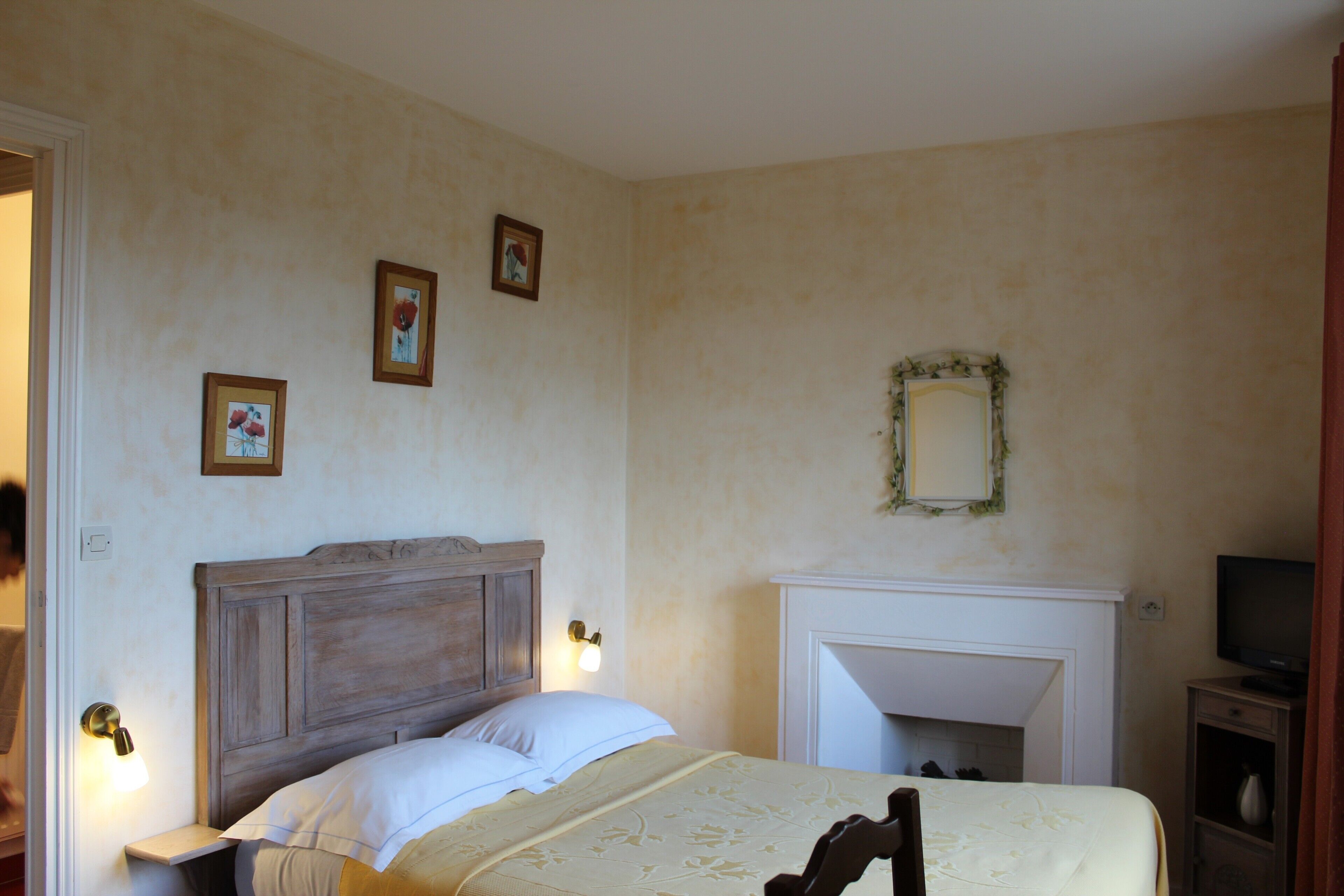 A bedroom with a wooden headboard, a bed with white linens, a fireplace, and a television on a stand.