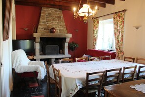 Un coin repas avec une cheminée, des chaises en bois, une table recouverte d’une nappe blanche et un téléviseur posé sur un meuble.