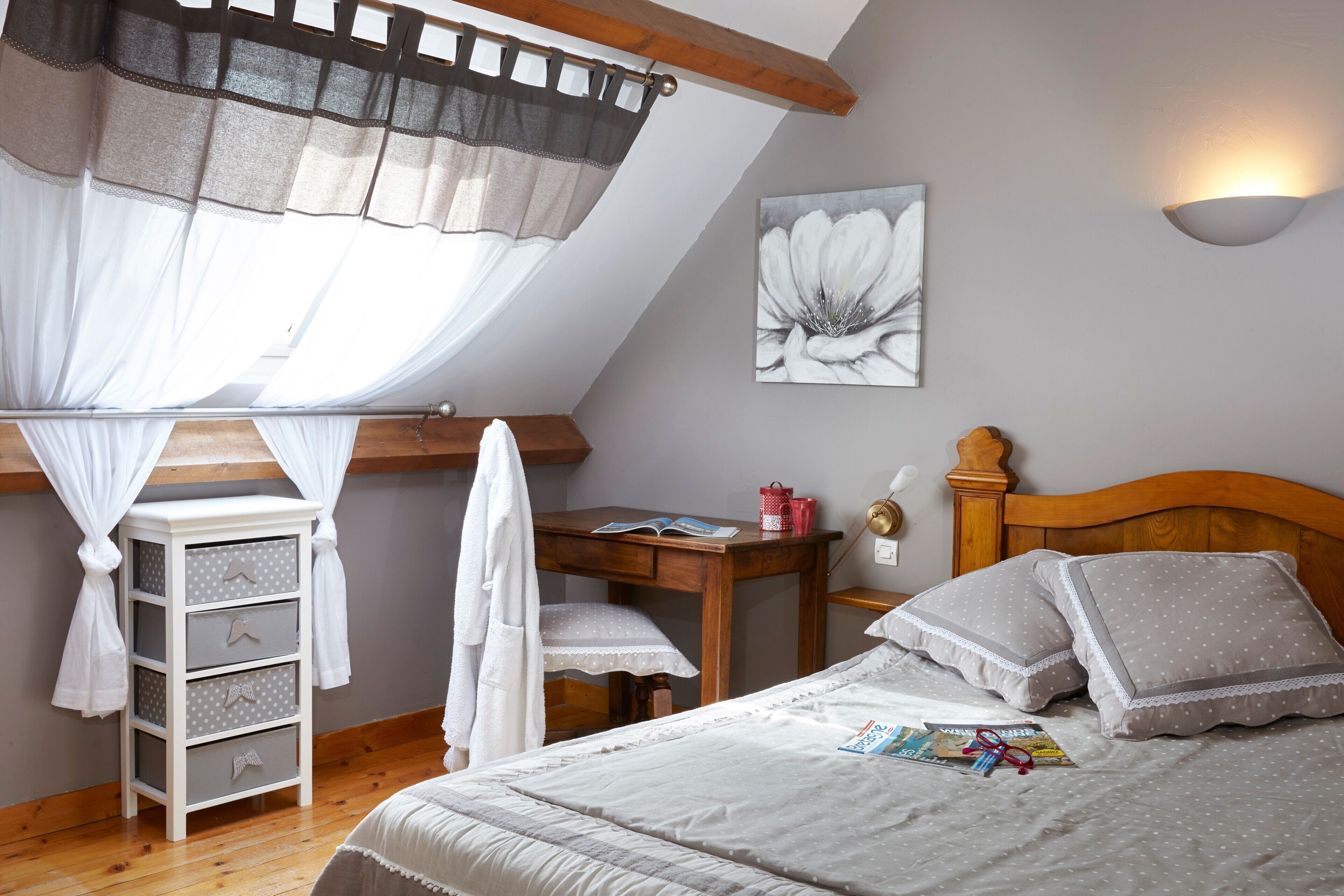 Een slaapkamer met een schuine kap, een houten bureau, een bed met kussens en een wandlamp.