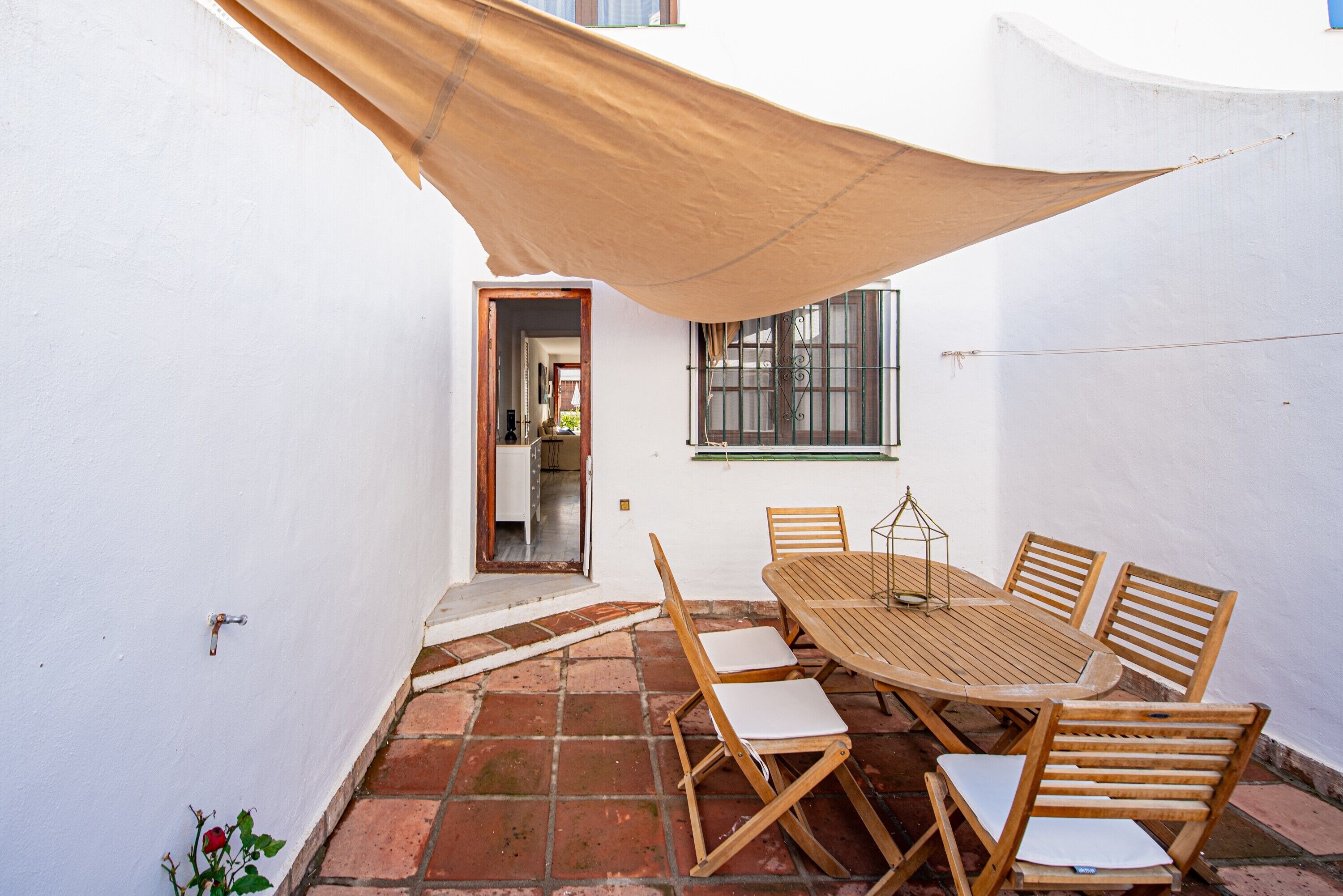 A patio with a wooden table and chairs, a hanging shade, and a window with metal bars.