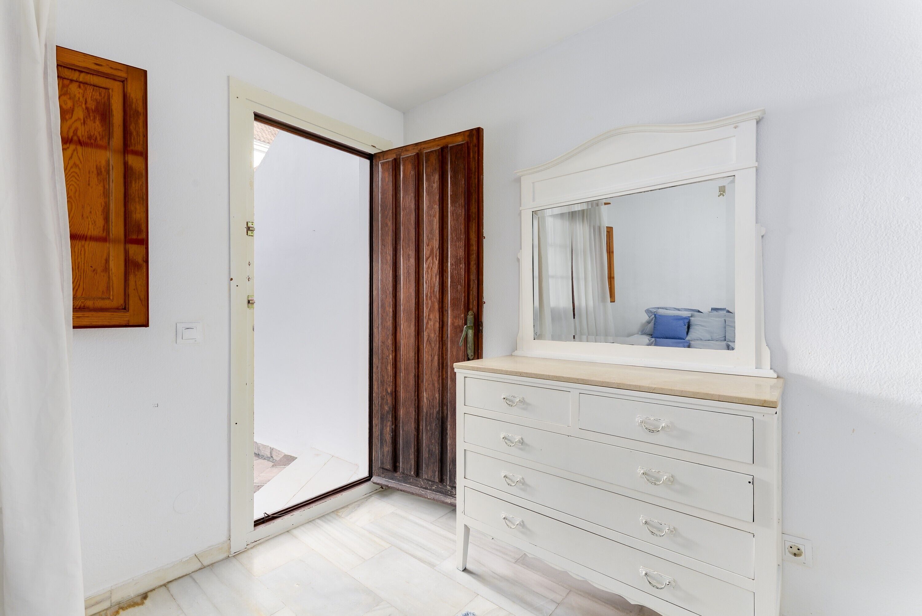 Een kamer met een witte kapstok, een houten deur en een spiegel die een blauw kussen weerspiegelt.