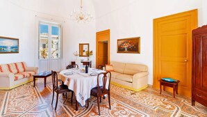Um quarto com uma mesa de jantar, cadeiras, um sofá, um candelabro e um tapete estampado.
