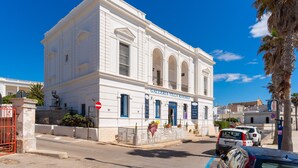 Um edifício branco com detalhes azuis, um letreiro com a inscrição 'GALLERIA VILLA RAMIREZ' e um sinal de estacionamento.