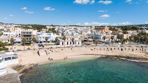 Uma cidade costeira com águas cristalinas, praia de areia e edifícios de arquitetura mediterrânea.